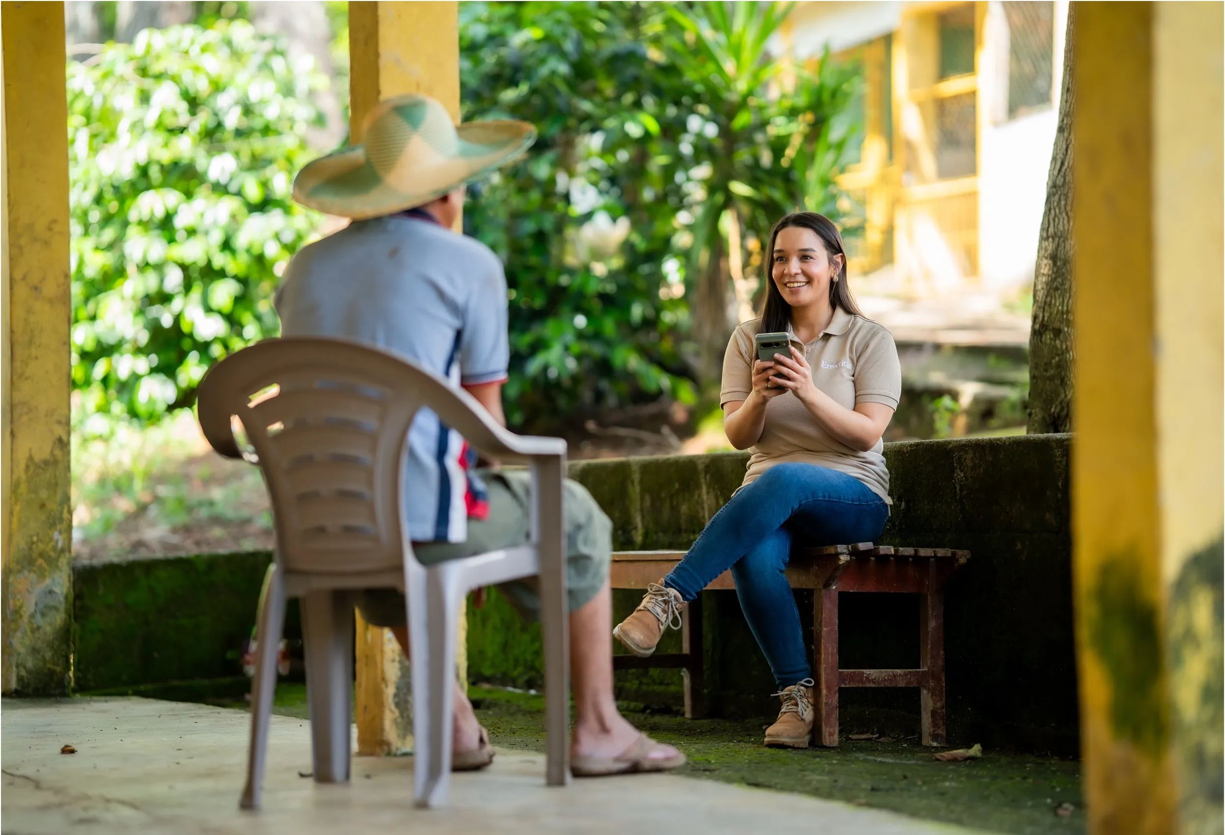 Woman smiling and holding a device while having running through a survey with a farmer.